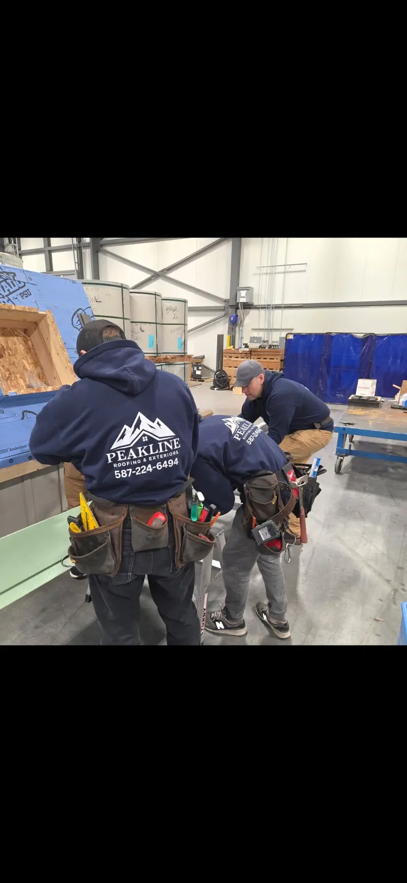 Two Peakline Roofing crew members in branded hoodies practicing installation techniques at training facility