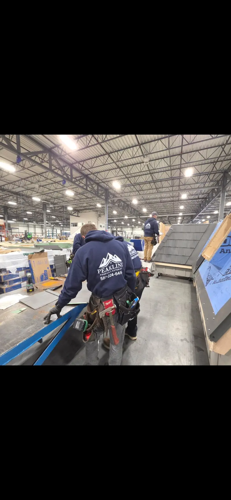 Peakline Roofing crew member in branded uniform walking through training facility with metal roofing mockup
