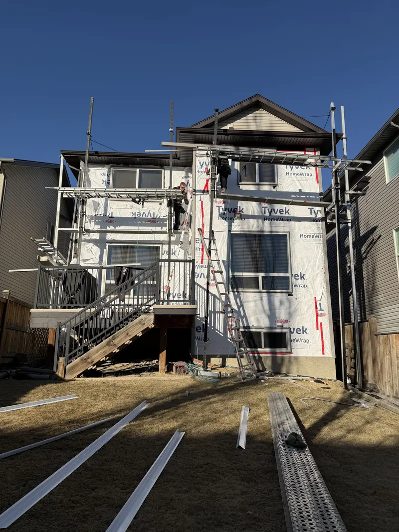 Two-storey Calgary home with Tyvek wrap and scaffolding during full siding replacement by Peakline Roofing & Exteriors